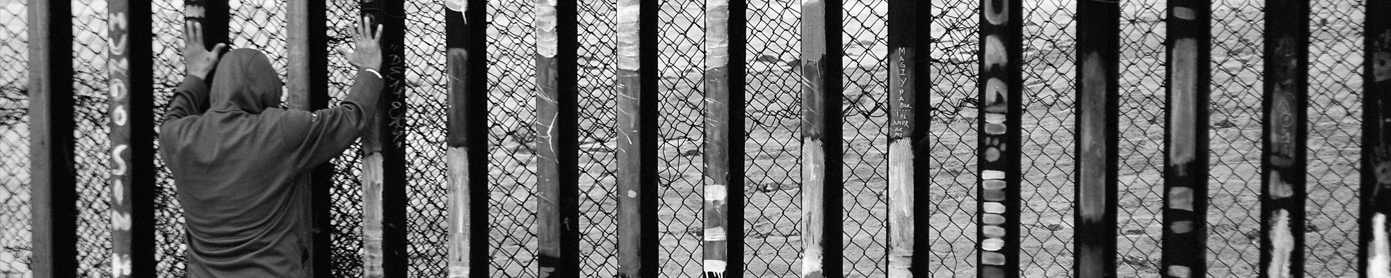 man standing with hands in the air facing border fence